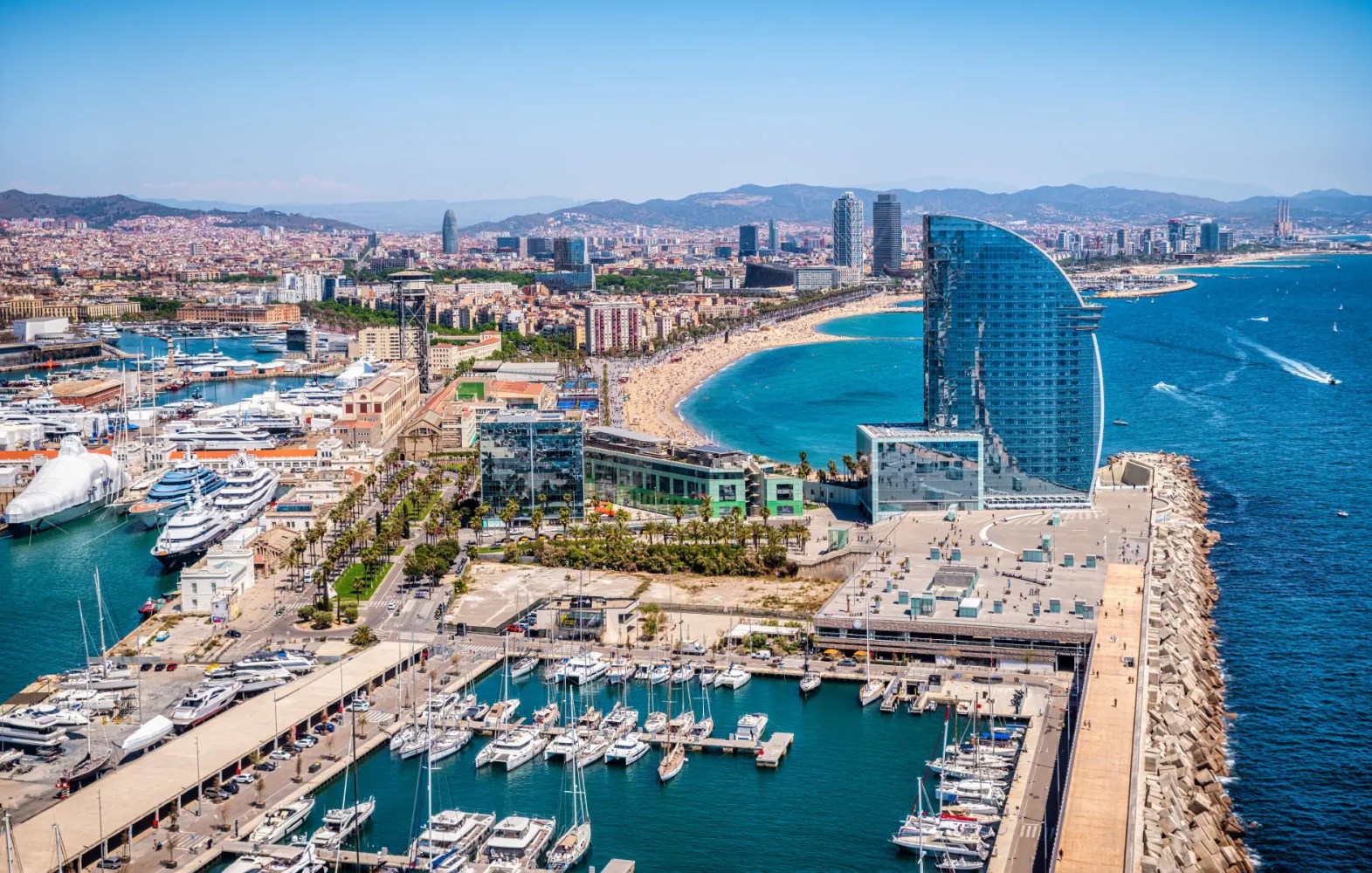 Aerial view of Barcelona coast with beach, marina, and modern skyscraper.