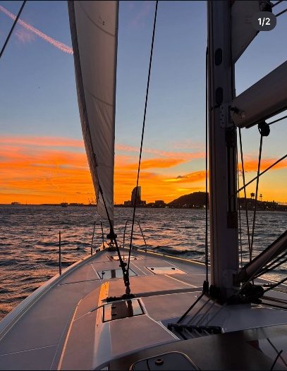Sailboat deck at sunset with orange sky and distant hills.