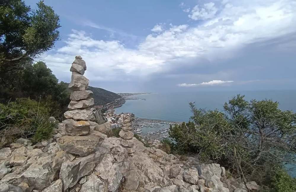 Stone cairns on a hill overlooking a coastal town and sea horizon.