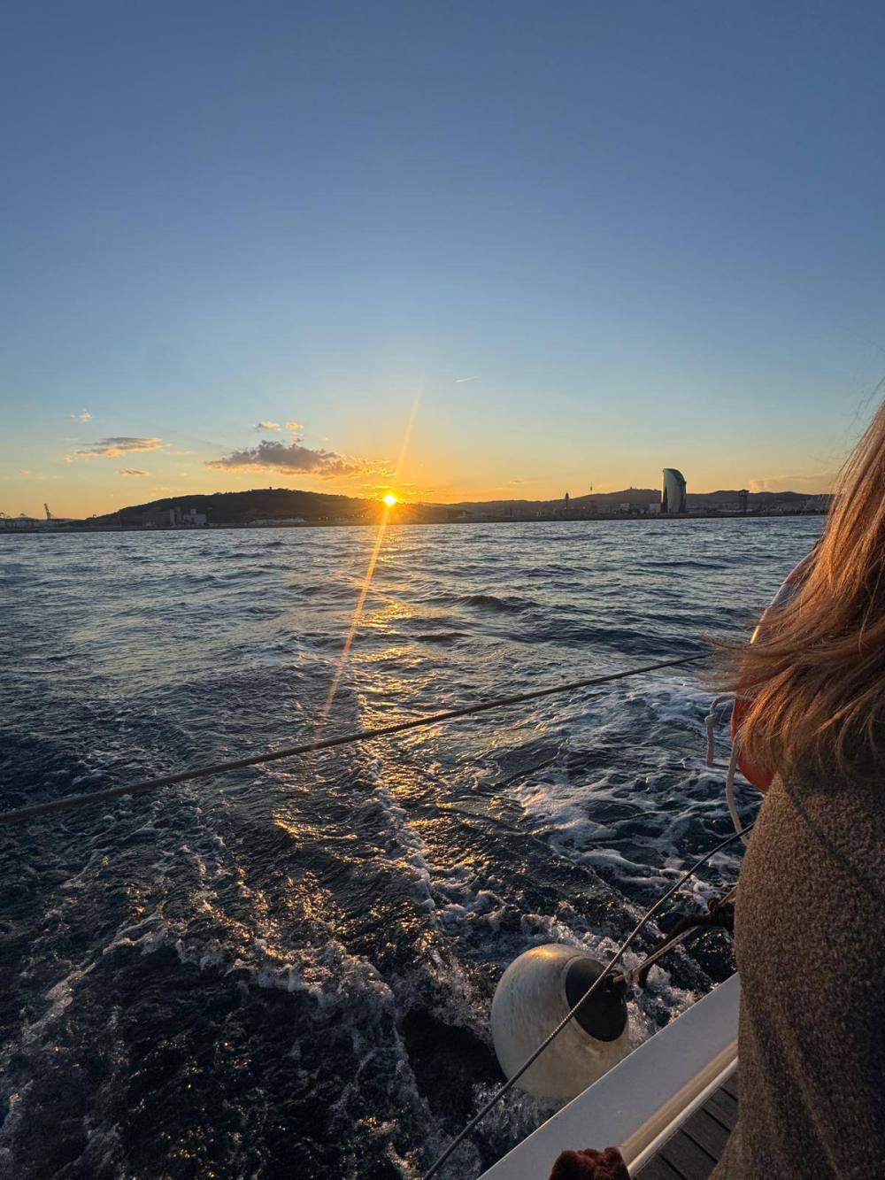 Sunset over the ocean, viewed from a boat's deck with railing and person on the right.